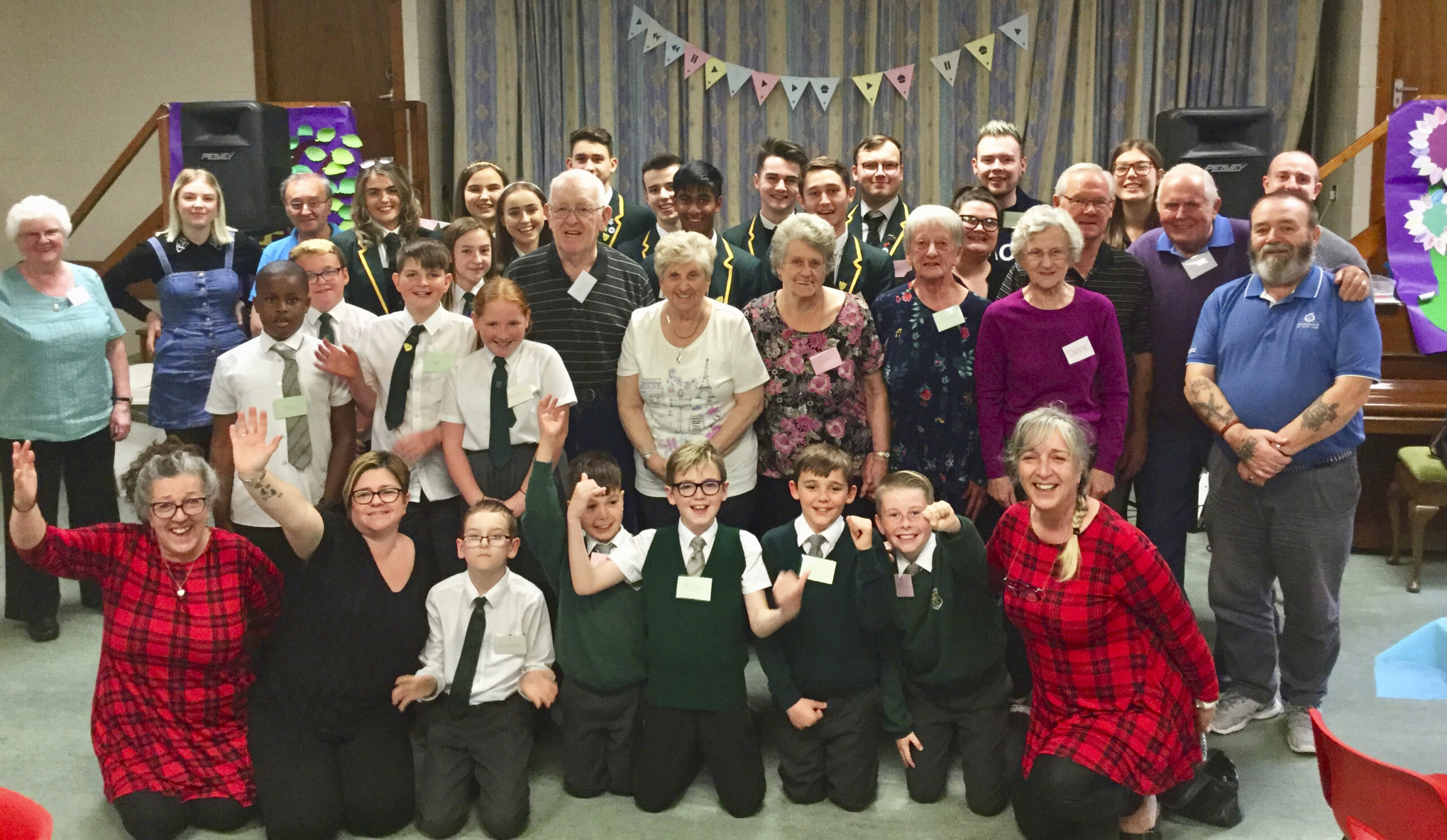 A group of about thirty people stand together in a Playlist for Help Point smiling towards the camera